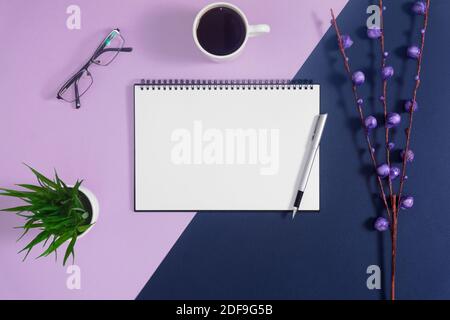 Vider la page du carnet en spirale et la tasse à café sur fond violet pastel et bleu. Banque D'Images