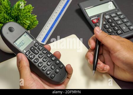 Mains tenant le téléphone et le stylo sur la table de travail du bureau. Banque D'Images
