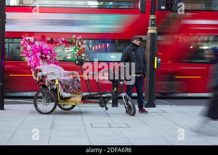 Un pousse-pousse, ou jinrikisha, décoré de fleurs, conducteur masculin en cuir veste et casquette de base ballon attendant le passager sur Londres West End, Angleterre Banque D'Images