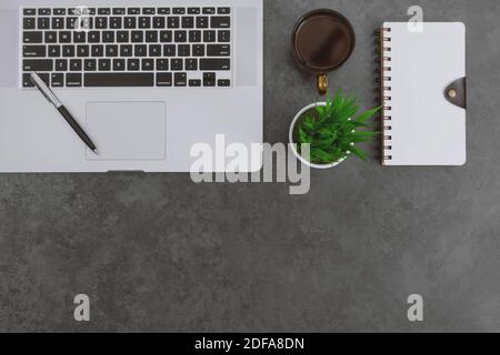 Vue sur le bureau avec ordinateur portable, ordinateur portable, stylo et plante en pot sur fond gris foncé. Banque D'Images