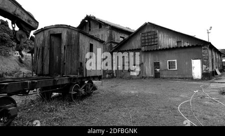 Vieux wagon pourri et rouillé abandonné debout à côté d'un Hangar abandonné [noir et blanc] Banque D'Images