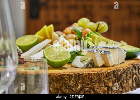 Trancher des fromages sélectionnés sur une planche de bois avec des raisins, de la chaux, de l'ananas et des herbes Banque D'Images