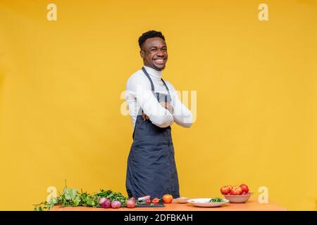 portrait d'un jeune chef africain souriant, avec quelques ingrédients pour un plat devant lui sur une table Banque D'Images