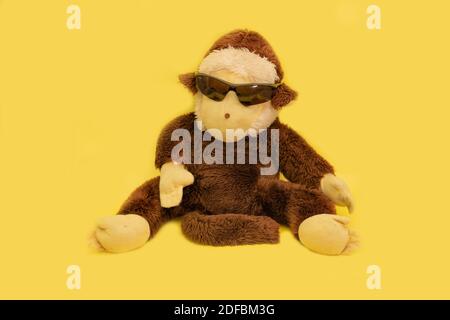 Singe en peluche avec lunettes de soleil sur fond jaune. Banque D'Images