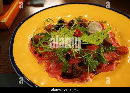 Gros plan carpaccio de bœuf avec salade de roquette, tomates séchées, olives noires et artichauts Banque D'Images