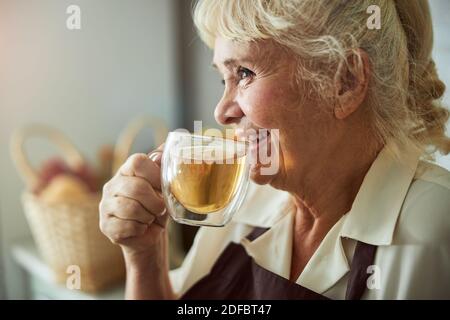 Une vieille femme joyeuse qui boit un délicieux thé frais à la maison Banque D'Images