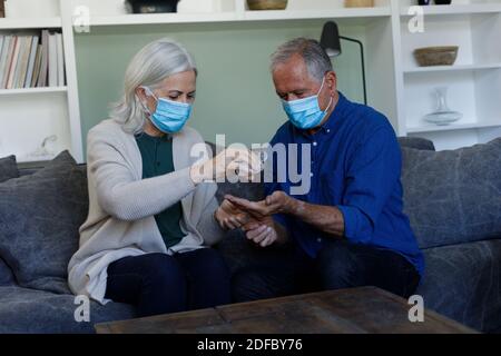 Couple caucasien âgé portant des masques faciaux utilisant un désinfectant pour les mains à accueil Banque D'Images