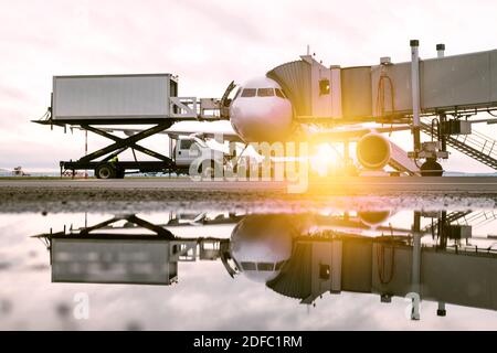 Manutention au sol d'un avion blanc près de la passerelle d'embarquement sous le soleil du matin. Chargement de la restauration à bord d'un camion à un avion Banque D'Images