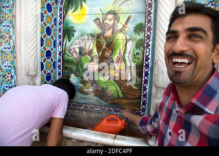 Iran, portrait d'un iranien prenant de l'eau d'une fontaine à Shiraz avec un portrait de Hazrat Abbas prenant de l'eau dans l'Euphrate Banque D'Images