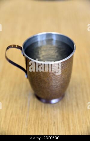 Un gros plan d'une tasse de cuivre remplie d'eau sur une surface en bois Banque D'Images