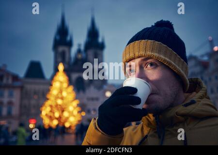 Un jeune homme buvant un punch contre un arbre de Noël. Place de la Vieille ville pendant l'avènement à Prague, République tchèque. Banque D'Images