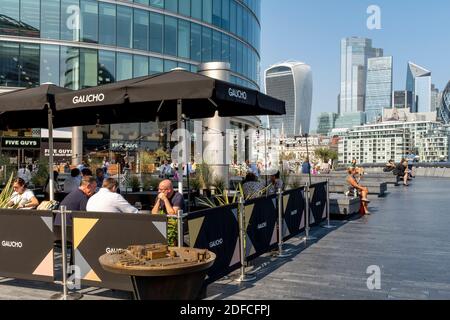 Les gens qui font leurs repas à l'extérieur au restaurant Gaucho (Tower Bridge) avec la City of London dans le Backround, London Bridge City Area, Londres, Royaume-Uni. Banque D'Images