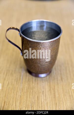 Un gros plan d'une tasse de cuivre remplie d'eau sur une surface en bois Banque D'Images