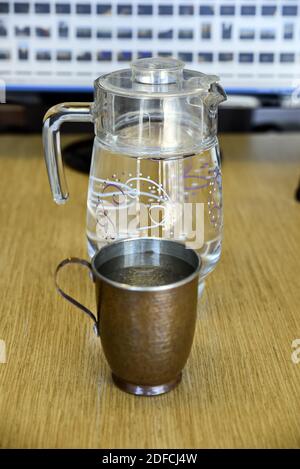 Un gros plan d'une tasse en cuivre avec une verseuse en verre rempli d'eau sur une surface en bois Banque D'Images