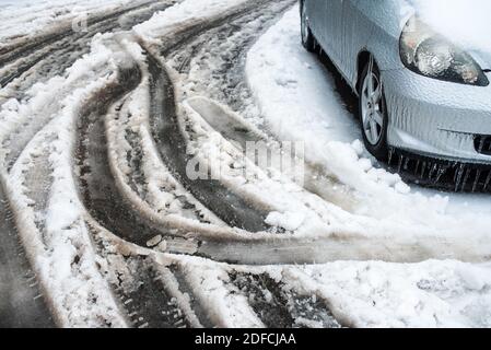 Traces des roues de voitures sur une route enneigée humide. Voiture couverte de glace, de neige et de glaçons. Ville en hiver. Temps de tempête de verglas. Banque D'Images