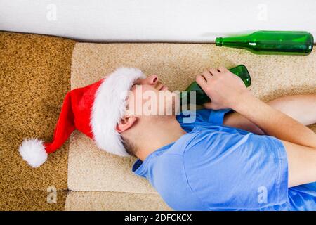 Un homme à Santa Hat dormant sur le canapé avec Une bière Banque D'Images
