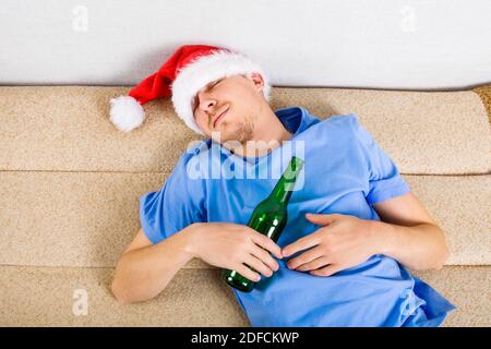 Jeune homme à Santa Hat dormir sur le canapé avec Une bouteille de bière Banque D'Images