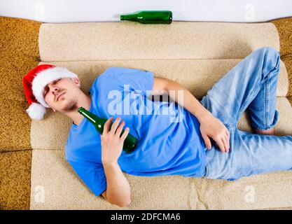 Un homme à Santa Hat dormant sur le canapé avec Une bière Banque D'Images