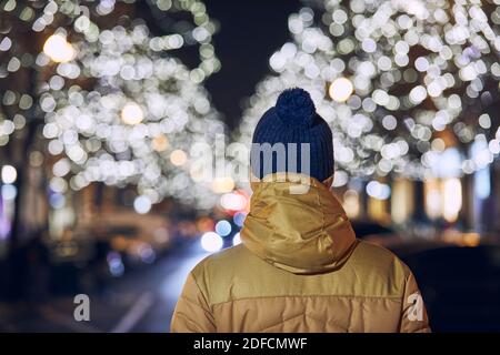 Vacances de Noël en ville. Vue arrière d'un jeune homme contre une rue éclairée avec des boutiques. Prague, République tchèque. Banque D'Images