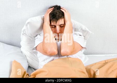 Un jeune homme ressent des maux de tête dans le lit à la maison Banque D'Images