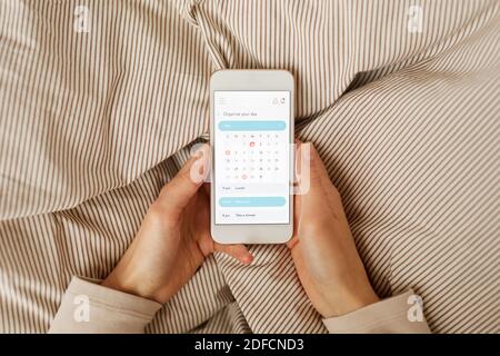 Gros plan d'une femme tenant un téléphone mobile et planifiant sa journée avec calendrier Banque D'Images