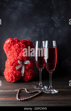 Deux verres de champagne rouge, sur fond sombre, un ours en peluche de roses. Cadeau pour femmes. Vacances des femmes. Banque D'Images