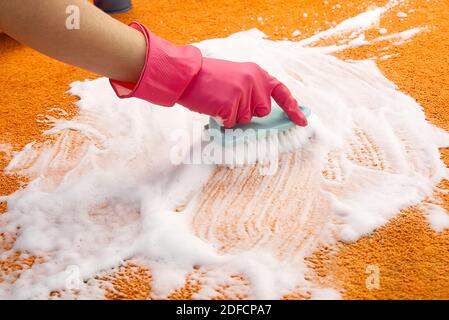 Femme nettoyage des mains taches sur le tapis avec une brosse dure. Nettoyage de tapis orange. Concept de service de nettoyage de tapis Banque D'Images