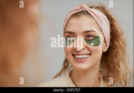 Jeune femme avec des taches sur son visage souriant à la miroir prenant soin de sa peau Banque D'Images