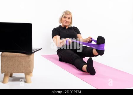 Femme âgée faisant de l'exercice avec une bande élastique. Formation en ligne en quarantaine. Banque D'Images