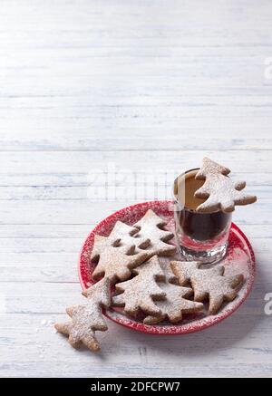 Biscuits au pain d'épice aux flocons d'avoine en forme d'arbre de Noël une assiette rouge arrosée de sucre en poudre avec un café prise de vue sur un arrière-plan bleu clair Banque D'Images