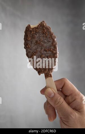 La main d'une femme tient un chocolat popsicle sticksavec un peu d'une morsure. Banque D'Images