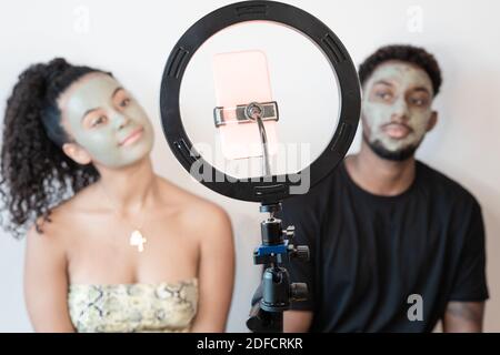 Couple d'influenceurs enregistrant des vidéos pour les fans. Portrait d'un couple marié avec des masques en argile verte sur leur visage. Concept de soins de beauté et de technologie. Banque D'Images