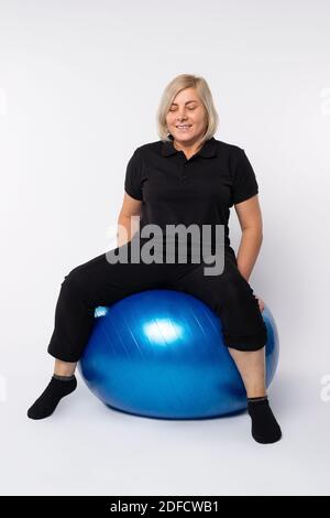 Femme sénior sur une balle de fitness après l'exercice. Arrière-plan blanc. Banque D'Images