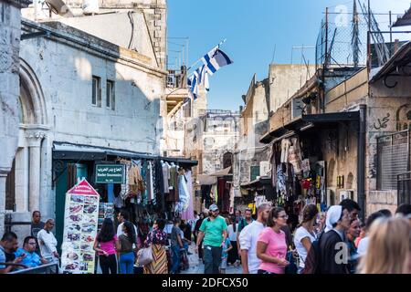Vue sur la rue avec beaucoup de touristes marchant sur les marchés à l'intérieur de la vieille ville de Jérusalem au Mont du Temple avec le fond des drapeaux nationaux israéliens. Banque D'Images