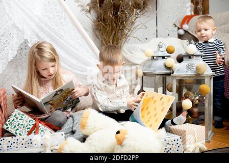 Trois enfants enfants lisent des livres entre les boîtes-cadeaux de Noël dans une maison décorée.Joyeux Noël et joyeuses fêtes! Banque D'Images