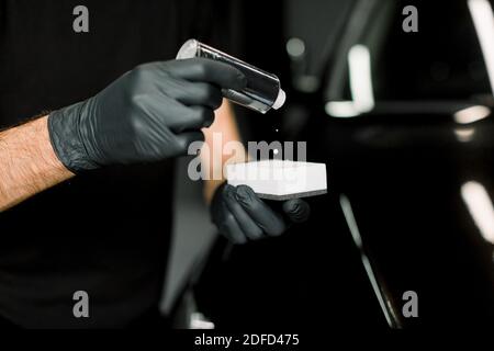 Image rognée des mains d'un ouvrier automobile masculin dans des gants de protection, application de crème à polir spéciale, revêtement en nano-céramique sur une éponge blanche, à Banque D'Images