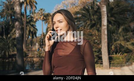 Belle fille parlant avec attention au téléphone avec un petit ami pendant la marche le long du parc de la ville Banque D'Images
