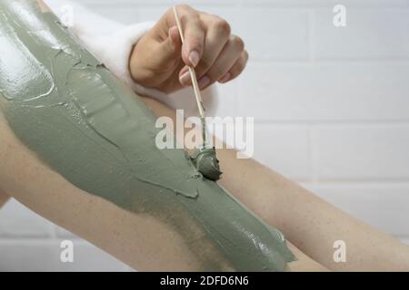 SPA, hydratant, traitement. Une femme applique un masque en argile avec une spatule sur la peau de ses jambes. Irritation après épilation, rasage. Soins de la peau à domicile Banque D'Images