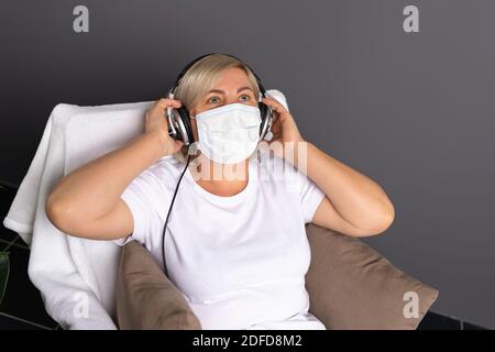 Une femme âgée portant un masque et de grands écouteurs écoute de la musique. Quarantaine. Banque D'Images