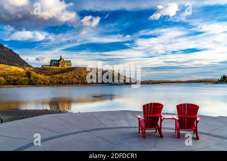 Chaise rouge, vue sur Waterton Lake Marina point en automne saison du feuillage matin ensoleillé. Ciel bleu avec des nuages colorés réfléchissent sur la surface de l'eau du lac Banque D'Images