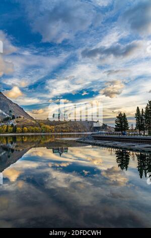 Parc national des Lacs-Waterton bord du lac en automne saison des feuillages matin. Ciel bleu, nuages colorés réfléchissent sur la surface du lac comme un miroir au lever du soleil. Banque D'Images