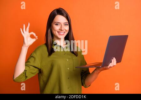 Photo portrait de jeune femme indépendante montrant l'ordinateur portable correctement geste souriant isolé sur un arrière-plan orange lumineux Banque D'Images