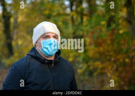 Jeune homme sérieux portant un masque de protection pendant le Coronavirus ou pandémie Covid-19 marchant dans les bois à l'automne un concept de la ne Banque D'Images