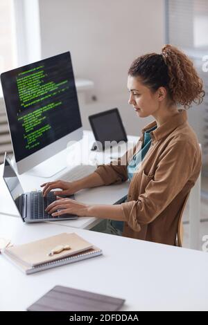 Jeune femme assise à la table et se concentrant sur en ligne travailler sur un ordinateur portable au service informatique Banque D'Images