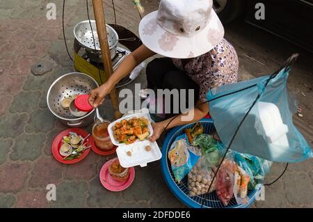 Phnom Penh, Cambodge - mars 2015 : femme au chapeau servant de la nourriture traditionnelle cambodgienne de rue. Femme mettant des aliments frits asiatiques dans une assiette en plastique. Frie Banque D'Images