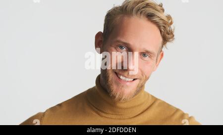 Beau barbu homme regardant avec plaisir dans la caméra sur fond blanc. Modèle masculin gai posé en studio Banque D'Images