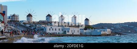 Mykonos, Grèce - 10 septembre 2019 : en time lapse, les touristes près de la « petite Venise » admirent le coucher du soleil. En arrière-plan les moulins à vent panoramiques. Banque D'Images