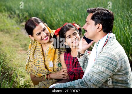 Bonne famille indienne d'agriculteur dans le domaine agricole en utilisant le téléphone Banque D'Images