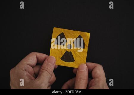 Homme tenant un panneau d'avertissement de rayonnement dans ses mains contre un fond noir. Touche Bas. Banque D'Images