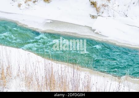 Rivière rugueuse au pied des montagnes dans une forêt turquoise, bleue, verte en hiver, de glace et de neige autour du paysage Banque D'Images